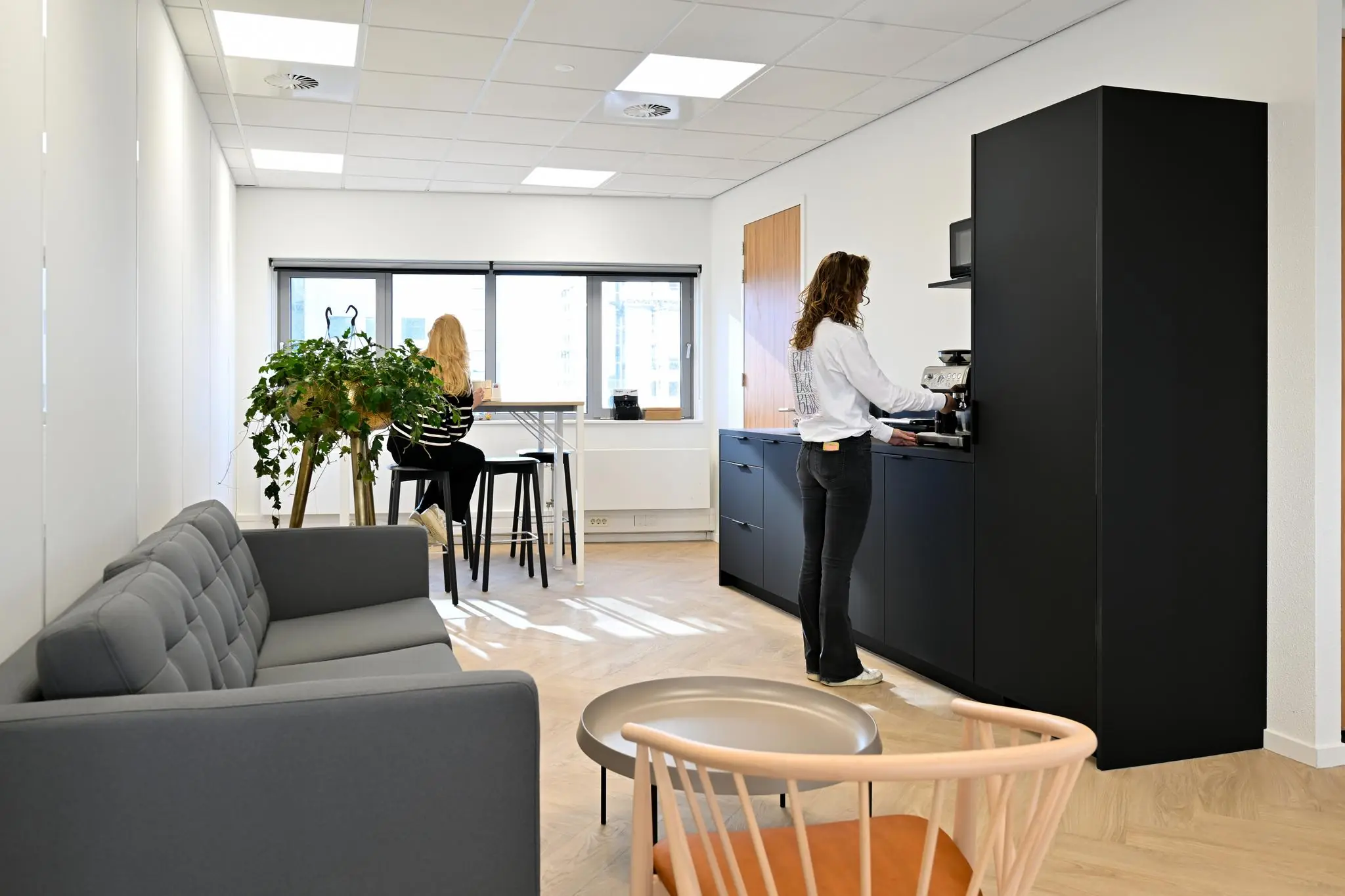 Moderne kantoorruimte in Rivium Quadrant met zithoek, koffieapparaat en twee vrouwen in een pantry.